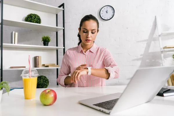 Привлекательная девушка смотрит на часы рядом ноутбук и яблоко — стоковое фото