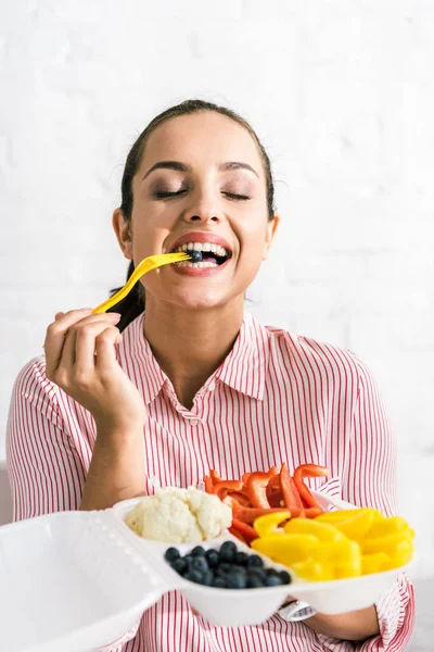 Mujer feliz sosteniendo tenedor de plástico con arándanos cerca de verduras - foto de stock