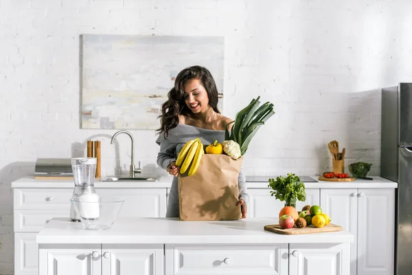 Cheerful woman standing near paper bag with tasty food — Stock Photo