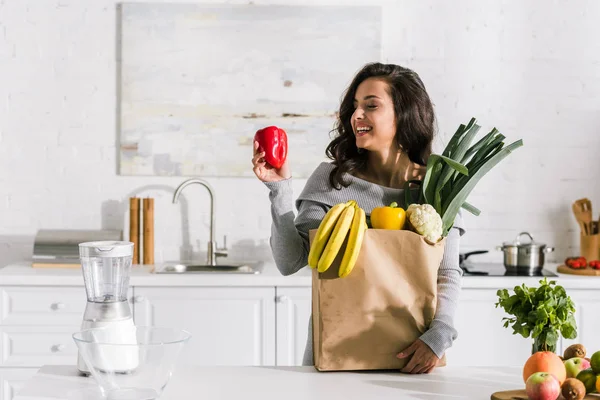 Happy girl looking at red paprika near paper bag — Stock Photo