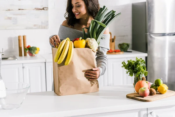 Fille heureuse regardant des bananes savoureuses dans un sac en papier — Photo de stock