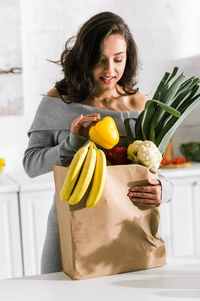 Cheerful girl looking at paper bag with groceries — Stock Photo