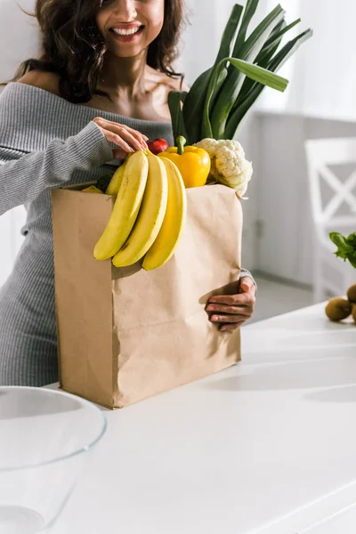 Vista recortada de la niña feliz sosteniendo bolsa de papel con comestibles - foto de stock