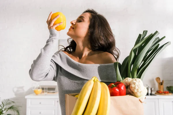 Happy girl smelling yellow paprika near bananas in paper bag — Stock Photo
