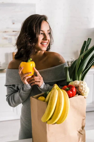 Mulher feliz segurando páprica amarela perto de mantimentos — Fotografia de Stock