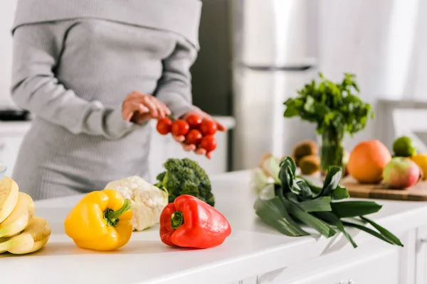 Селективный фокус свежих овощей рядом с женщиной на кухне — стоковое фото