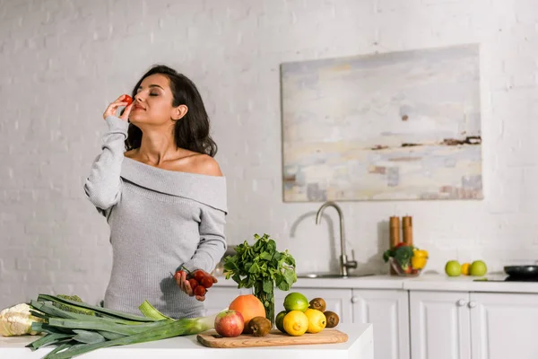 Attractive girl smelling cherry tomato near vegetables — Stock Photo