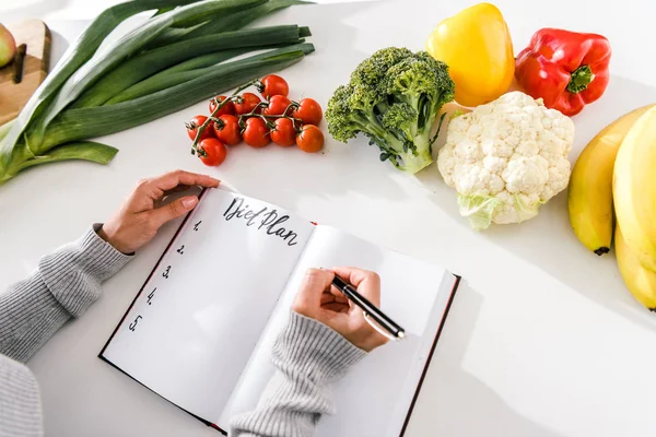 Vista recortada de la mujer escribiendo en cuaderno con plan de dieta - foto de stock