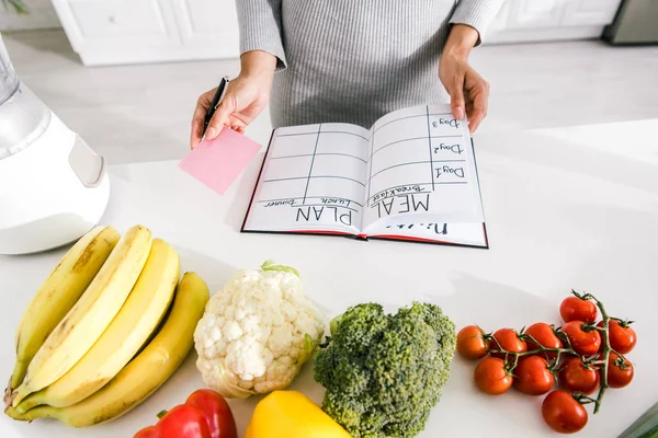 Vue recadrée d'une femme près d'un ordinateur portable avec plan de repas et légumes sur la table — Photo de stock