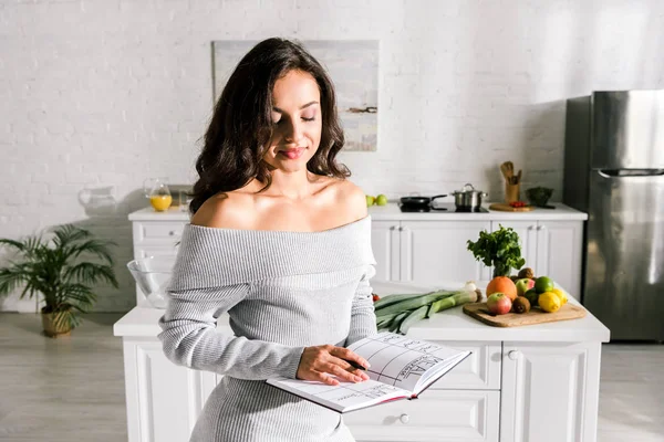 Chica atractiva sosteniendo cuaderno con letras en la cocina - foto de stock