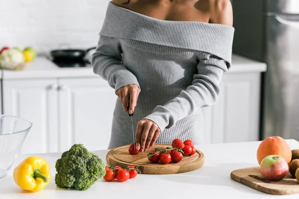 Vista cortada da mulher segurando faca perto de tomates cereja vermelhos e frutas — Fotografia de Stock