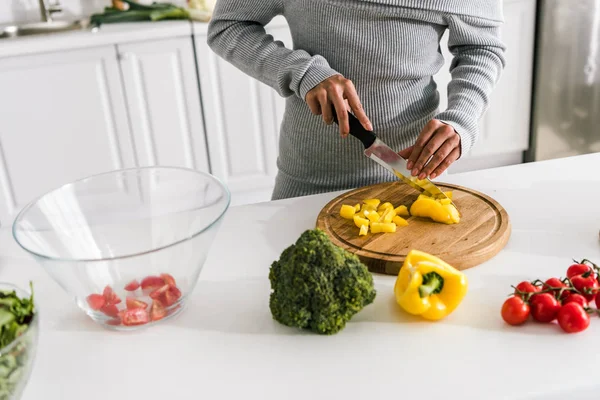 Cropped view of woman cutting yellow paprika near cherry tomatoes and broccoli — Stock Photo