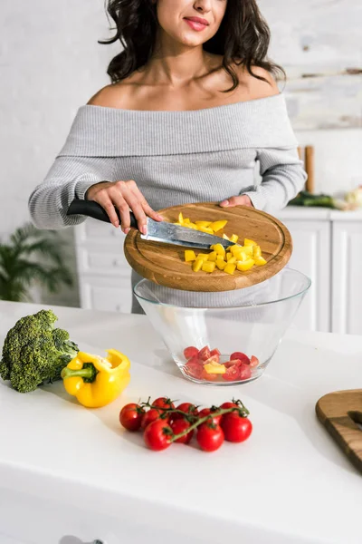 Cropped view of woman putting sliced yellow paprika in glass bowl — Stock Photo