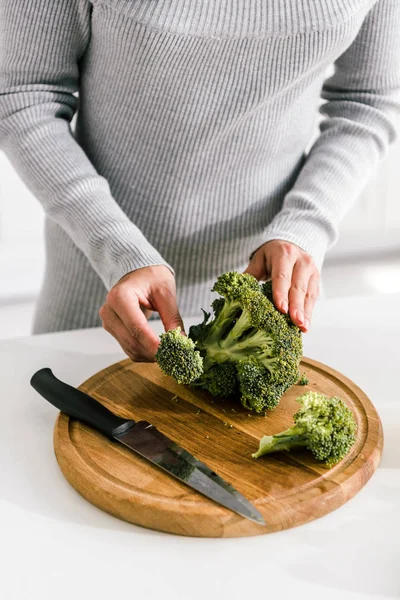 Cropped view of woman standing near cutting board with green broccoli — Stock Photo