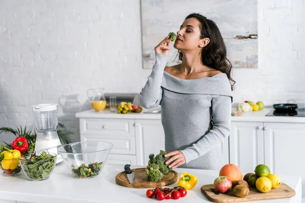 Attractive girl smelling broccoli near vegetables and glass bowls — Stock Photo