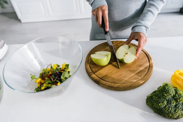 Vista recortada de mujer sosteniendo cuchillo cerca de mitades de manzana - foto de stock