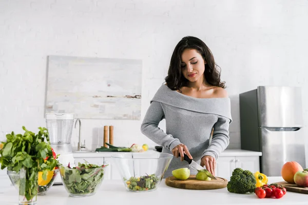 Chica atractiva sosteniendo cuchillo mientras se corta manzana - foto de stock