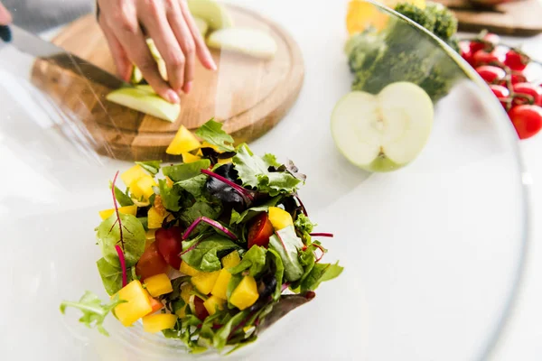 Selective focus of glass bowl with salad near woman cutting apple — Stock Photo