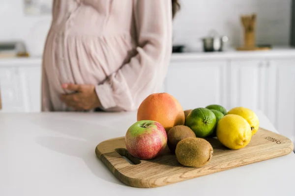 Cropped view of pregnant woman touching belly near fruits on table — Stock Photo