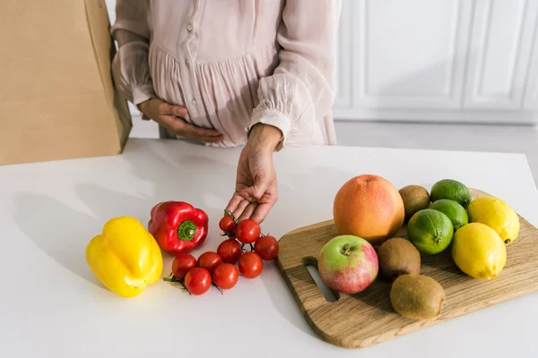 Vista recortada de la mujer embarazada tocando tomates rojos cereza - foto de stock