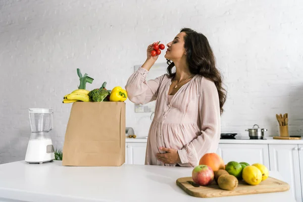 Happy woman smelling cherry tomatoes near groceries — Stock Photo