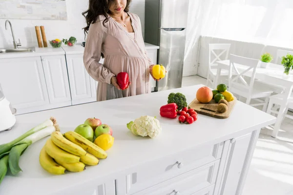 Abgeschnittene Ansicht einer schwangeren Frau, die Paprika in der Nähe von leckerem Essen auf dem Tisch hält — Stockfoto