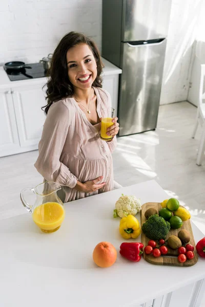 Vista aérea de la mujer embarazada feliz sonriendo mientras sostiene el vaso con jugo de naranja - foto de stock