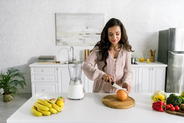 Atractiva mujer embarazada corte pomelo cerca de verduras y frutas - foto de stock