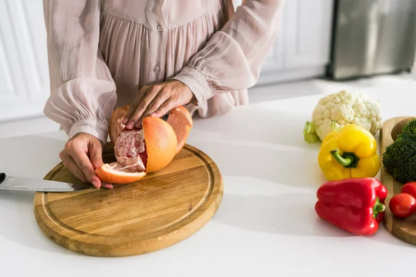 Обрезанный вид беременной женщины, чистящей грейпфрут рядом с овощами — стоковое фото