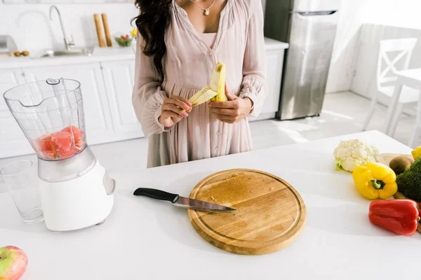 Vista recortada de la mujer embarazada pelando plátano cerca de licuadora con pomelo - foto de stock