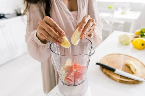 Vista recortada de la mujer embarazada poniendo plátano en la licuadora con pomelo - foto de stock