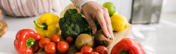Panoramic shot of woman touching kiwi near vegetables — Stock Photo