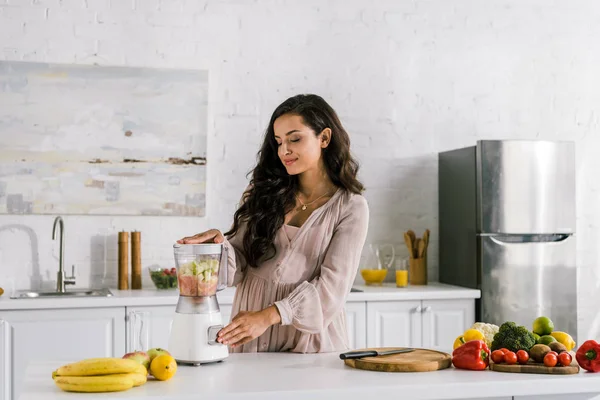 Glücklich schwangere Frau berührt Knopf auf Mixer mit Früchten — Stockfoto