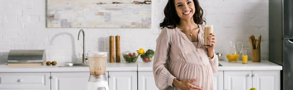 Tiro panorâmico de mulher feliz tocando barriga e segurando saboroso smoothie — Fotografia de Stock