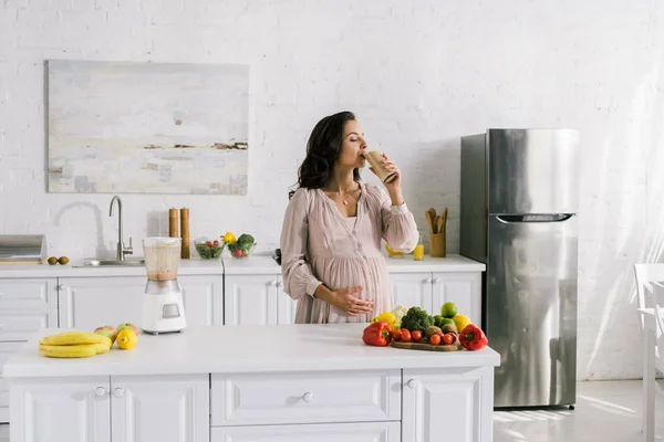 Беременная женщина пьет смузи возле стола с вкусной едой — стоковое фото