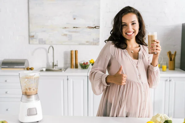 Heureux femme enceinte montrant pouce vers le haut et tenant verre avec smoothie — Photo de stock