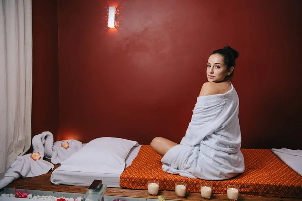 Attractive woman in bathrobe sitting on massage mat in spa salon — Stock Photo