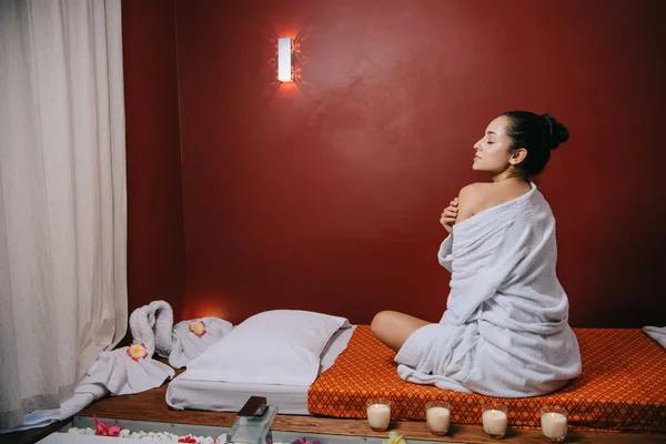 Attractive woman in bathrobe sitting on massage mat in spa salon — Stock Photo