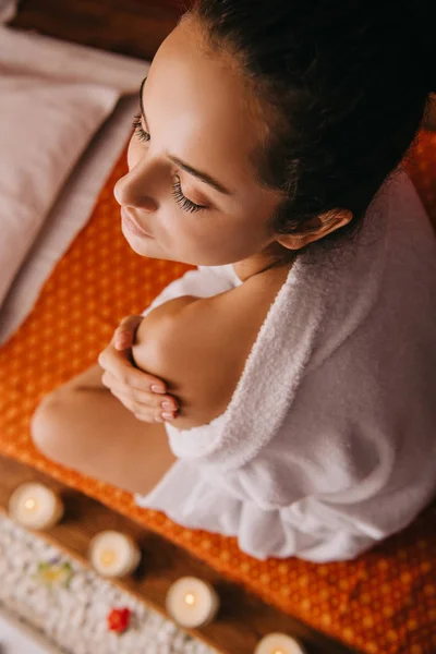 Vista de alto ângulo da mulher atraente em roupão de banho sentado no tapete de massagem no salão de spa — Fotografia de Stock