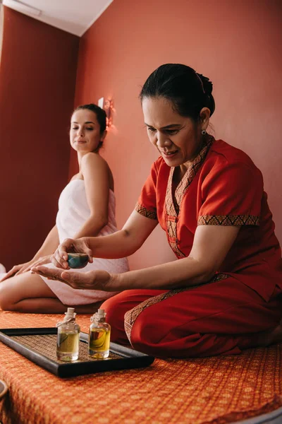 Selective focus of asian masseur pouring fragrance oil on hand — Stock Photo