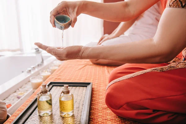 Vista recortada del masajista vertiendo aceite de fragancia en la mano - foto de stock