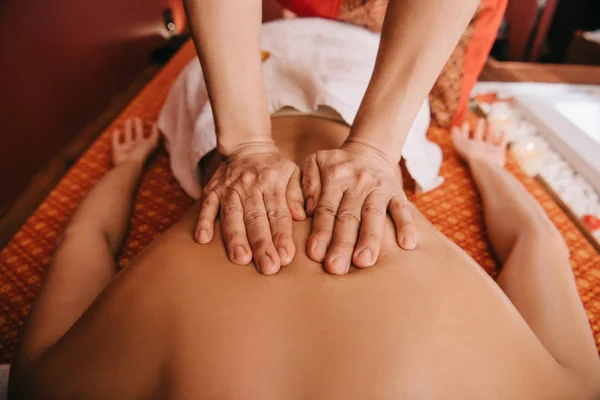 Vista cortada de massagista fazendo massagem nas costas para a mulher no tapete de massagem — Fotografia de Stock