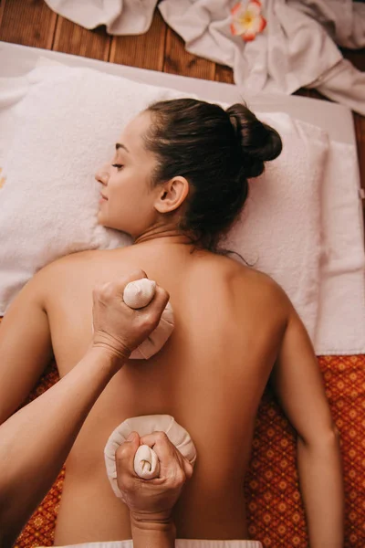 Vue recadrée de masseur faisant massage du dos avec des boules à base de plantes à la femme dans le spa — Photo de stock