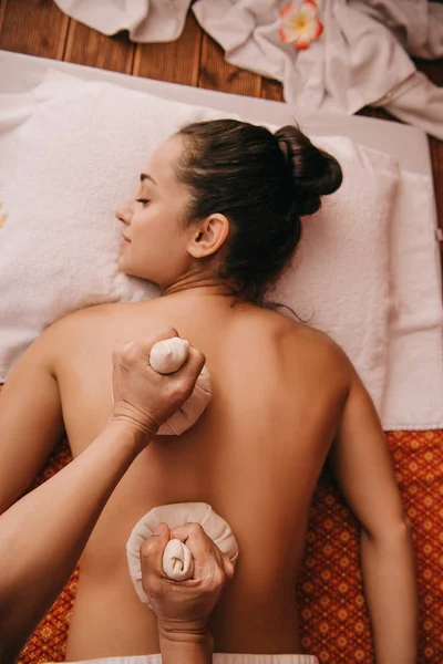 Vista recortada de masajista haciendo masaje de espalda con bolas de hierbas a la mujer en spa - foto de stock