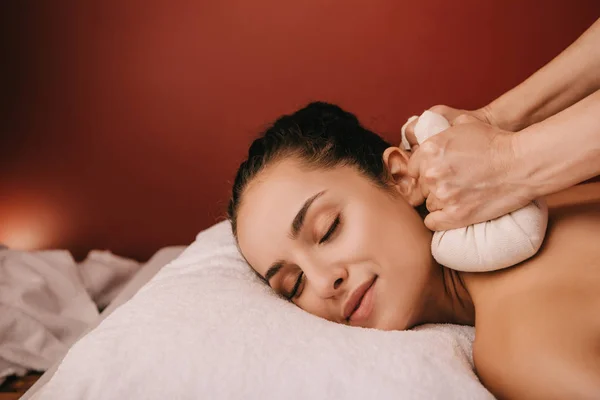 Vista ritagliata di massaggiatore facendo massaggio alla schiena con le palle di erbe per la donna in spa — Foto stock