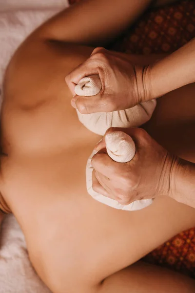 Vista recortada de masajista haciendo masaje de espalda con bolas de hierbas a la mujer en spa - foto de stock