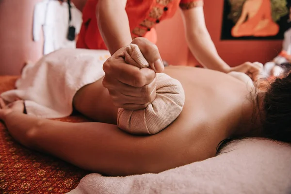 Vista recortada de masajista haciendo masaje de espalda con bolas de hierbas a la mujer en spa - foto de stock