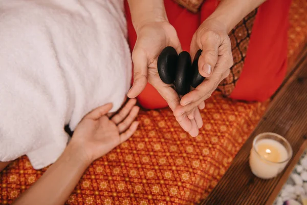 Vista recortada de masajista sosteniendo piedras calientes para masaje - foto de stock