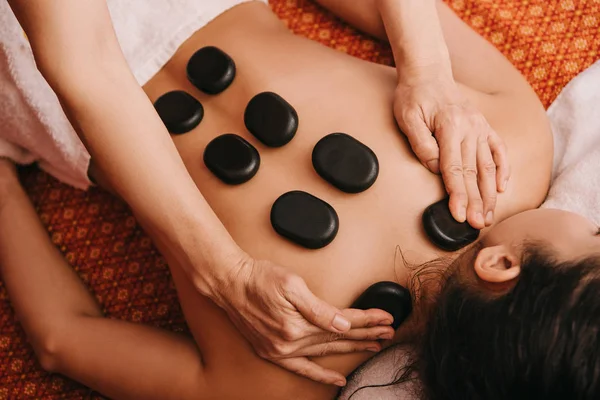 Vista recortada de masajista haciendo masaje de piedra caliente a la mujer en el salón de spa - foto de stock