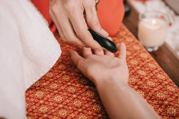 Vista ritagliata del massaggiatore facendo massaggio con pietre calde alla donna nel salone spa — Foto stock